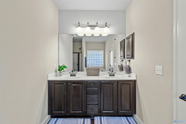 bathroom with double vanity, a shower stall, baseboards, and a sink