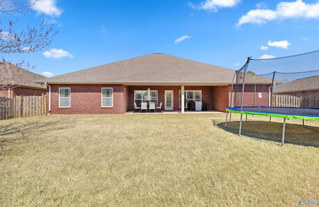 back of property with a patio, a trampoline, fence, a yard, and brick siding