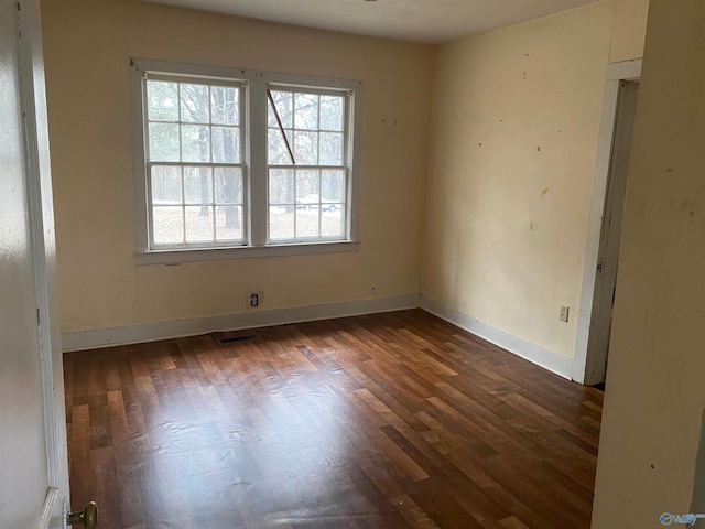 unfurnished room with visible vents, dark wood finished floors, and baseboards