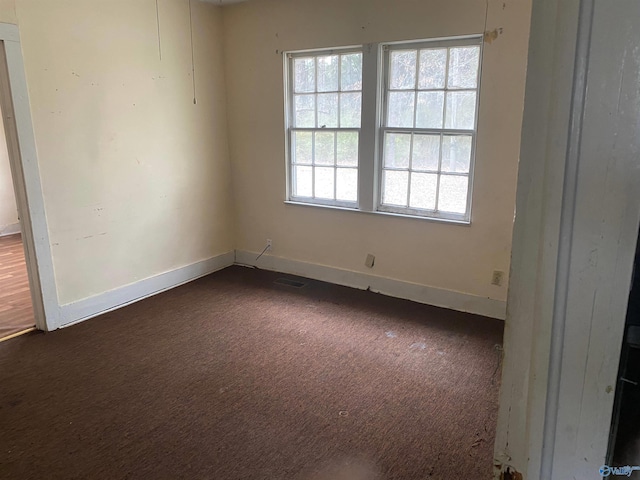 empty room with dark colored carpet, visible vents, and baseboards