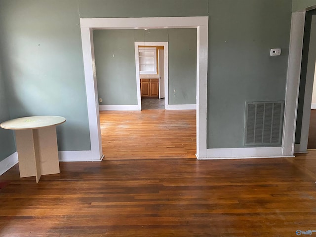 empty room with dark wood-type flooring, visible vents, and baseboards