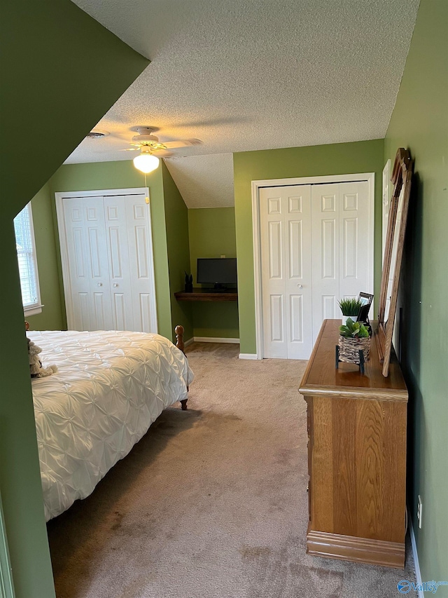 carpeted bedroom with a textured ceiling, two closets, and ceiling fan