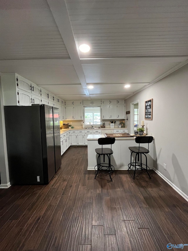 kitchen with dark wood-type flooring, white cabinets, black fridge, a kitchen bar, and kitchen peninsula