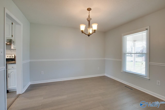 empty room with a chandelier, a textured ceiling, and light hardwood / wood-style flooring