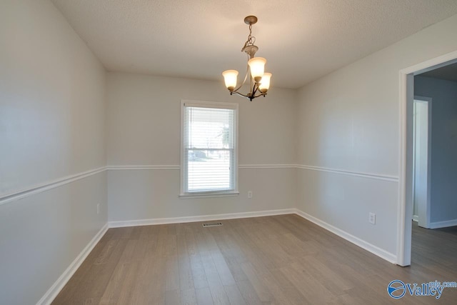 spare room with a chandelier, a textured ceiling, and hardwood / wood-style flooring