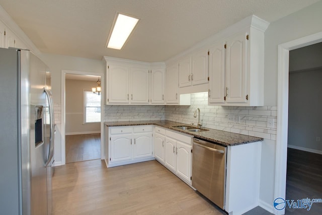 kitchen featuring appliances with stainless steel finishes, light wood-type flooring, sink, dark stone countertops, and white cabinetry