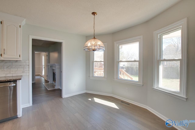 unfurnished dining area with a chandelier, a textured ceiling, light wood-type flooring, and a healthy amount of sunlight