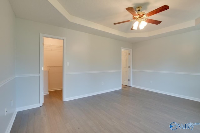 unfurnished room featuring a raised ceiling, ceiling fan, and wood-type flooring