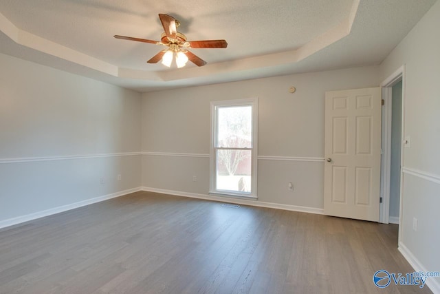 empty room featuring a raised ceiling, ceiling fan, a textured ceiling, and light wood-type flooring