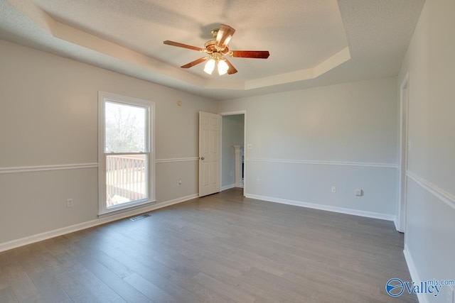 empty room with a raised ceiling, ceiling fan, a textured ceiling, and hardwood / wood-style flooring