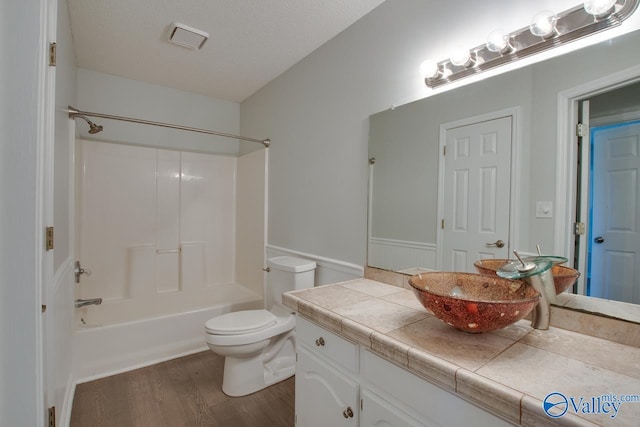 full bathroom with shower / bathing tub combination, vanity, hardwood / wood-style flooring, toilet, and a textured ceiling