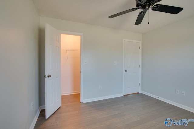 unfurnished bedroom featuring a walk in closet, a closet, light hardwood / wood-style flooring, and ceiling fan