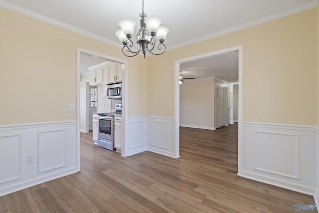 unfurnished dining area featuring wainscoting, ceiling fan with notable chandelier, crown molding, and wood finished floors