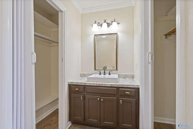 bathroom featuring baseboards, wood finished floors, ornamental molding, and vanity