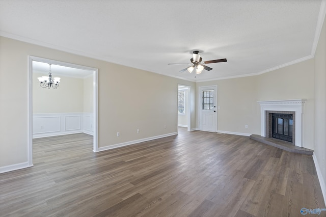 unfurnished living room with ceiling fan with notable chandelier, crown molding, wood finished floors, and a fireplace