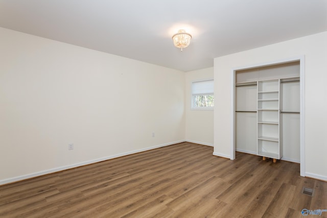 unfurnished bedroom featuring a closet, dark hardwood / wood-style flooring, and a chandelier