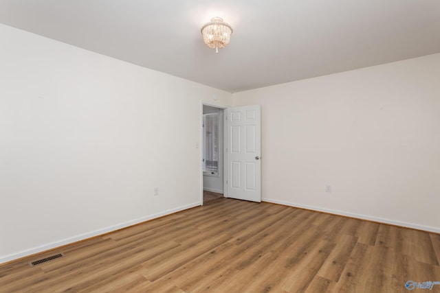 unfurnished room featuring a chandelier and light hardwood / wood-style flooring