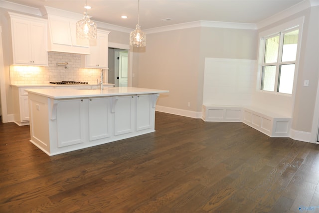 kitchen with dark hardwood / wood-style floors, tasteful backsplash, white cabinetry, an island with sink, and hanging light fixtures