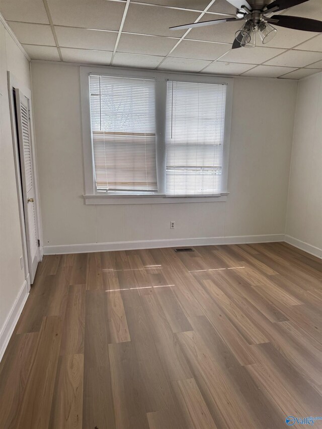 empty room with ceiling fan, a drop ceiling, baseboards, and wood finished floors