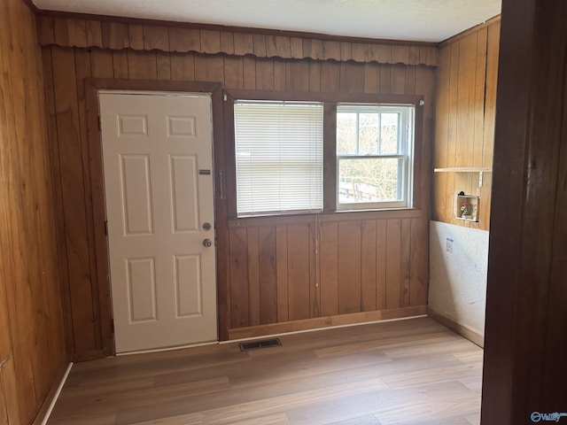 foyer entrance featuring visible vents, baseboards, light wood-style floors, and wood walls