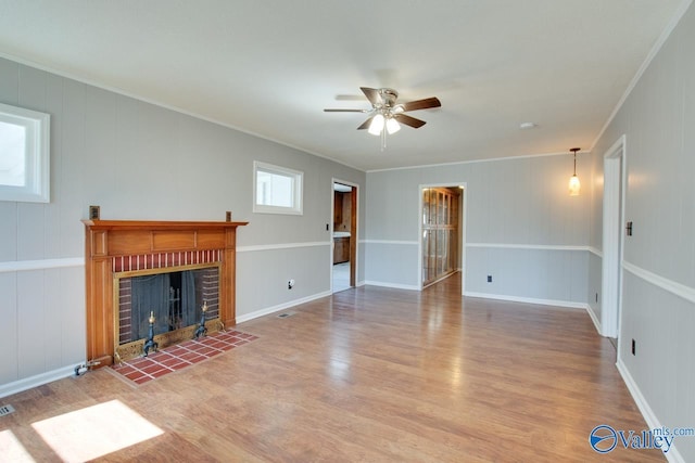 unfurnished living room with a fireplace, ornamental molding, ceiling fan, wood finished floors, and baseboards