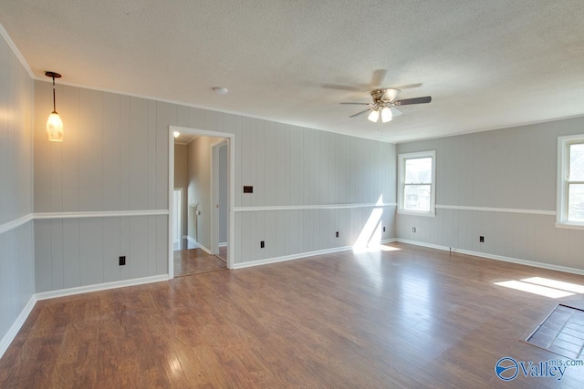 empty room with a ceiling fan, ornamental molding, a textured ceiling, wood finished floors, and baseboards