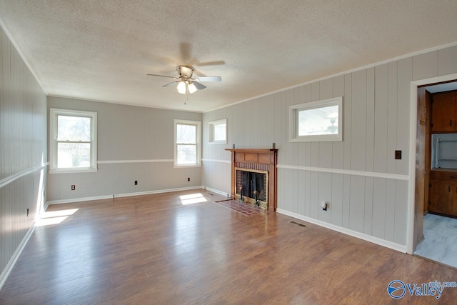 unfurnished living room featuring visible vents, ornamental molding, a brick fireplace, ceiling fan, and wood finished floors