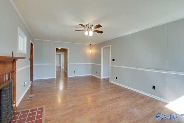 unfurnished living room with visible vents, a fireplace with flush hearth, ornamental molding, ceiling fan, and wood finished floors