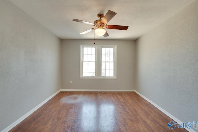 spare room with visible vents, dark wood-type flooring, a ceiling fan, and baseboards