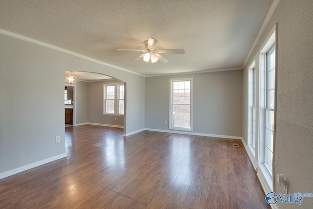 empty room with ornamental molding, arched walkways, dark wood finished floors, and a textured ceiling