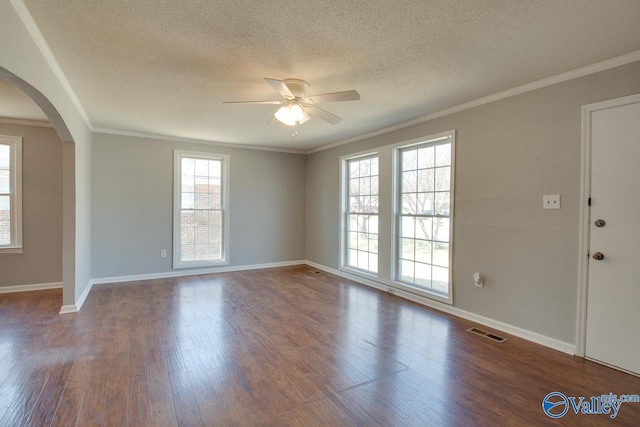 unfurnished room with arched walkways, wood finished floors, visible vents, baseboards, and crown molding