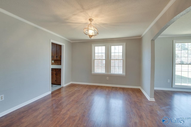 empty room featuring arched walkways, dark wood-type flooring, ornamental molding, a textured ceiling, and baseboards