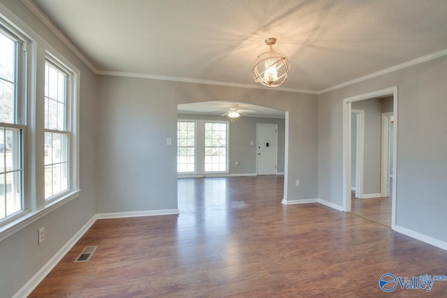 unfurnished room with arched walkways, dark wood-style flooring, visible vents, and a healthy amount of sunlight