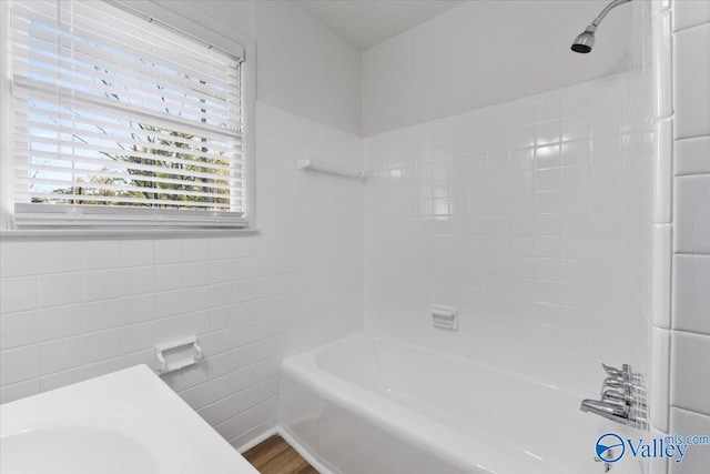 bathroom with hardwood / wood-style flooring, tiled shower / bath combo, and tile walls