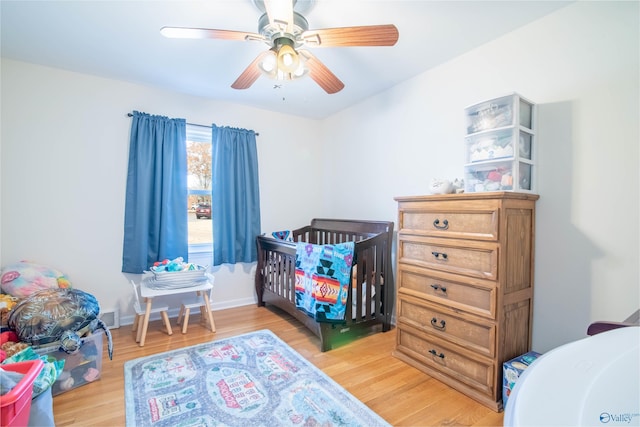 bedroom featuring a crib, light hardwood / wood-style flooring, and ceiling fan