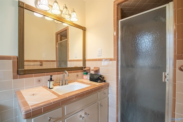 bathroom with a shower with door, vanity, and tile walls