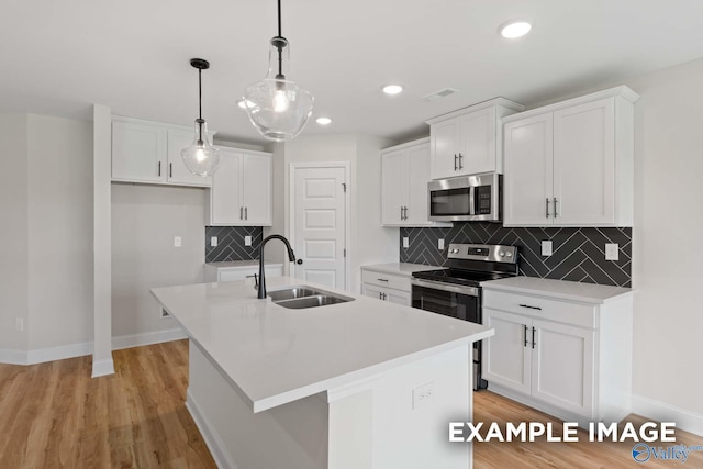 kitchen with stainless steel appliances, an island with sink, pendant lighting, and white cabinetry