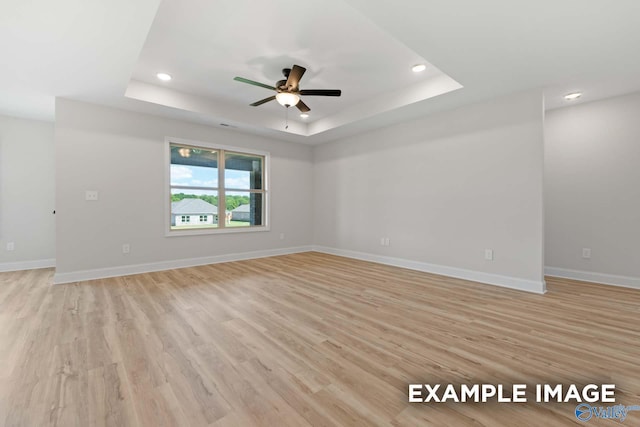 unfurnished room with ceiling fan, a tray ceiling, and light hardwood / wood-style flooring