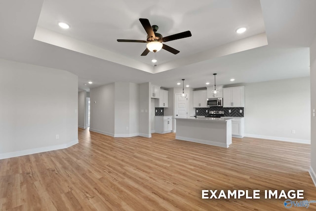 kitchen featuring a center island, a raised ceiling, pendant lighting, stainless steel appliances, and white cabinets