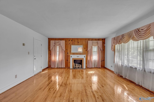 unfurnished living room with wooden walls, light hardwood / wood-style floors, and a tile fireplace