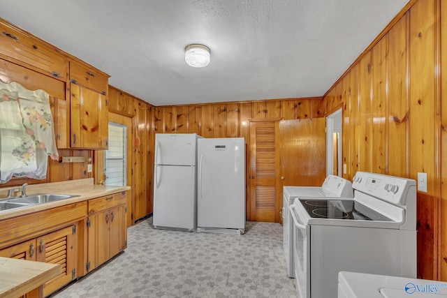 kitchen featuring sink, wood walls, white fridge, and washing machine and clothes dryer