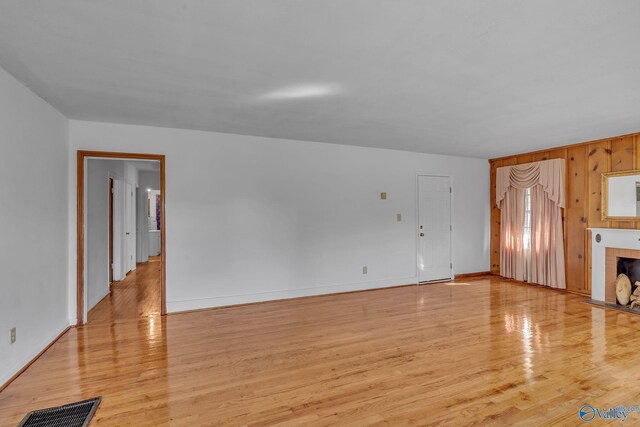 1013 Hermosa Ave, Gadsden, AL 35901 - unfurnished living room featuring light wood-style floors, visible vents, wood walls, a tile fireplace, and baseboards