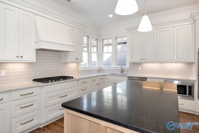 kitchen featuring white cabinets, appliances with stainless steel finishes, custom exhaust hood, and a sink