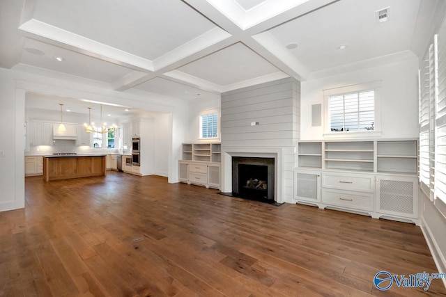 unfurnished living room with a wealth of natural light, dark wood finished floors, a fireplace, and an inviting chandelier