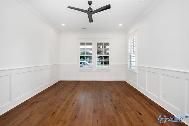 empty room featuring a wainscoted wall, wood-type flooring, a ceiling fan, and a healthy amount of sunlight