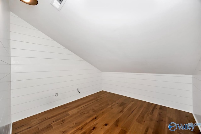 bonus room featuring dark wood-style flooring, lofted ceiling, visible vents, and wood walls