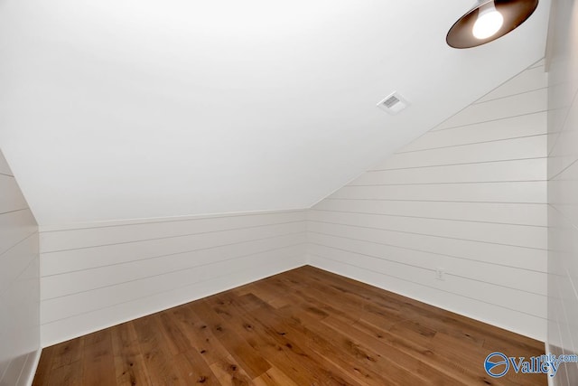 bonus room with lofted ceiling, wood walls, visible vents, and hardwood / wood-style flooring