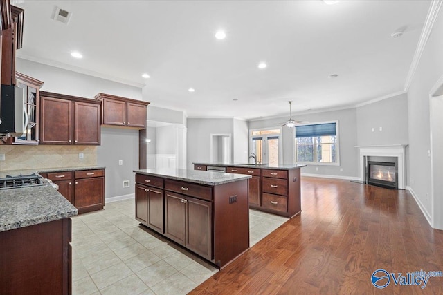 kitchen with sink, light stone counters, a center island, ornamental molding, and decorative backsplash