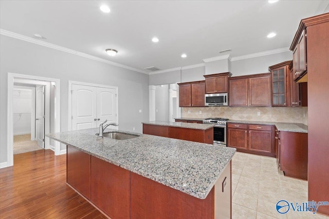 kitchen featuring sink, tasteful backsplash, stainless steel appliances, light stone countertops, and a kitchen island with sink