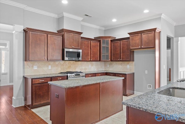 kitchen featuring light stone countertops, decorative backsplash, stainless steel appliances, and a center island